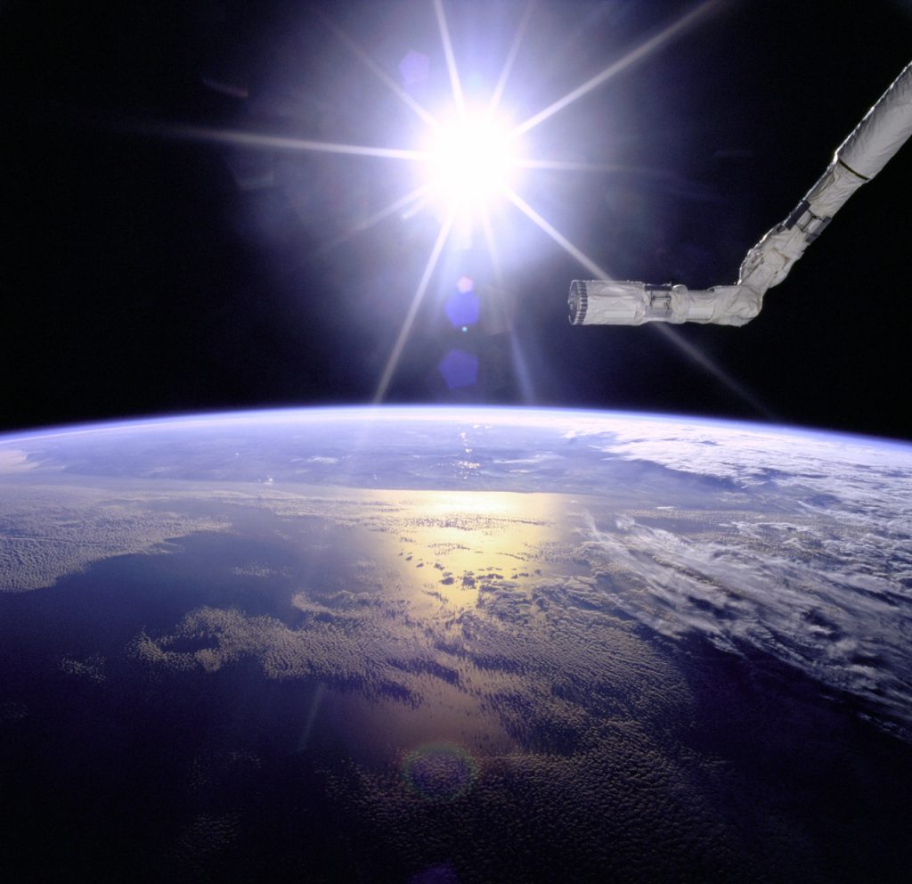 View of the Remote Manipulator System (RMS) end effector over an Earth limb with a solar starburst pattern behind it